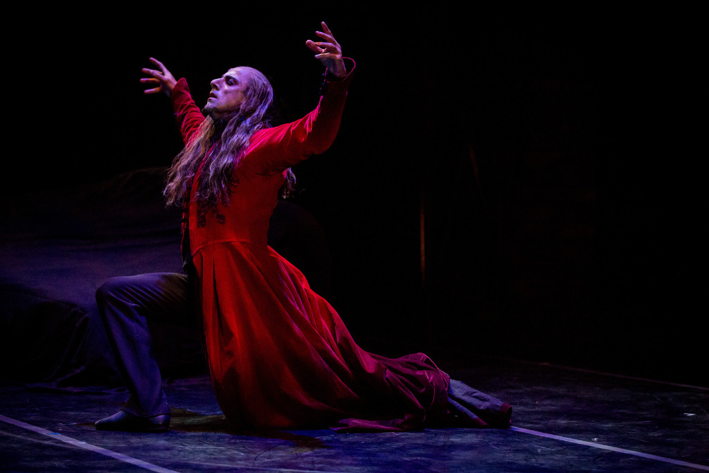 man with red cloak reaching arms up while lunging